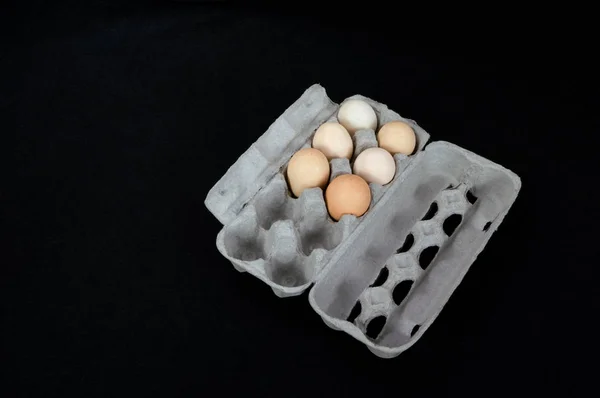 Cardboard egg box with six eggs on black felt background.