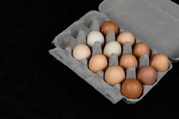 Twelve chicken eggs in a carton box, isolated on black felt background.