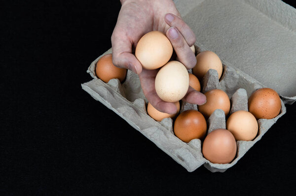 Man holding two eggs in his hand, taken from a cardboard egg box on black felt background.