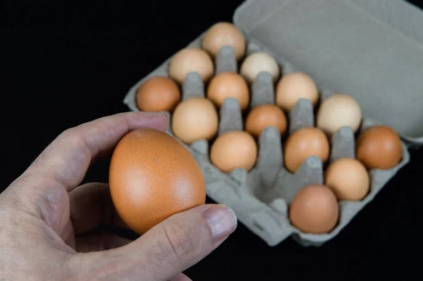 Man holding one egg in his hand, taken from a cardboard egg box on black felt background.