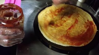 Cook siyah bir ocak üzerine krep bazı domates sosu koyarak