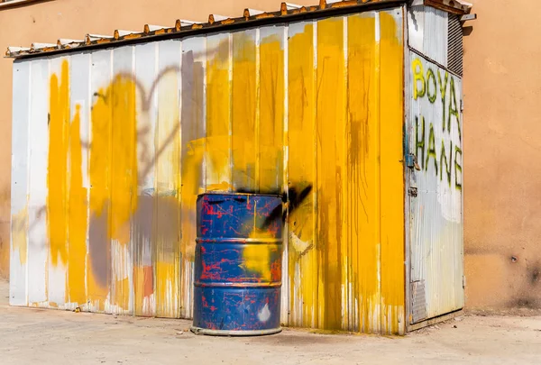 Blue metal drum in front of a shed painted in white and yellow.