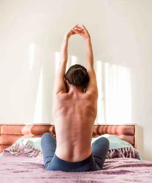Back view of a Caucasian half-naked woman waking up in bed and stretching her muscles
