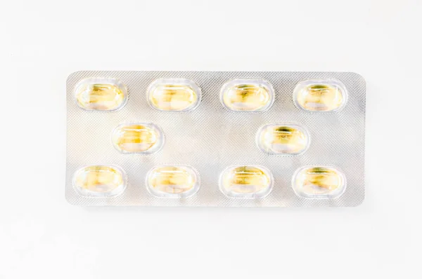 Dez cápsulas amarelas acondicionadas numa embalagem blister isolada em bcakground branco — Fotografia de Stock