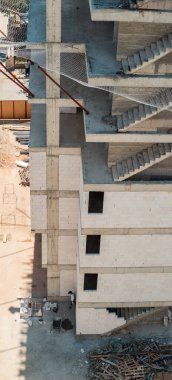 İnşaat halindeki bir binanın yüksek açılı görüntüsü bitmemiş beton merdivenler ve inşaat alanının güvenlik ağı ağır kazmaları kaldırabilir..