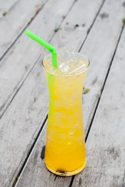 Juice mango and passion fruit drink yellow color in tall glass with straw green color on wooden terrace