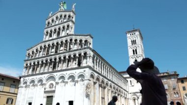 Lucca, İtalya, Temmuz 2018 - Hasır şapkalı kadın silueti Foro, Lucca 'da San Michele' in fotoğrafını çekiyor. St. Michael kilisesini ziyaret eden kadın gezgin, İtalya 'nın Toskana kentinin Roma katedrali önünde yürüyen turist.