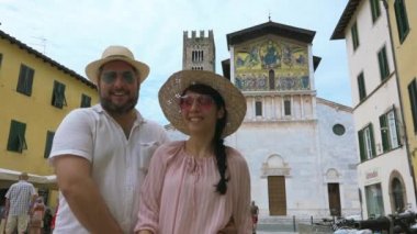 Lucca, İtalya, Temmuz 2018 gülümseyen bir çift San Frediano kilisesi önünde selfie çekip öpüşüyorlar, Lucca. Mutlu insanlar Toskana 'ya, eski anıtlarıyla neşeli turistlere, İtalya' da fotoğraf tatiline gidiyor.