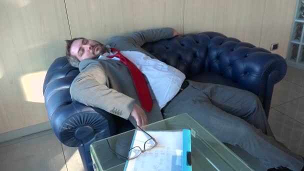 三十多岁的商人睡在工作场所 辛苦工作 压力很大的生活方式 疲惫的高加索人在行政办公室的沙发上睡着了 疲倦的首领在蓝色的沙发上打盹 — 图库视频影像