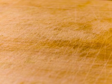 Açık kahverengi tahta kesim tahtasının detaylı makro fotoğrafı sayısız bıçak izi ve çizik gösteriyor. Aşınmış doku, mutfak veya mutfak temalı tasarımlar için ideal otantik bir rustik arkaplan oluşturarak, yemek hazırlamada sık sık kullanıldığını vurgular..