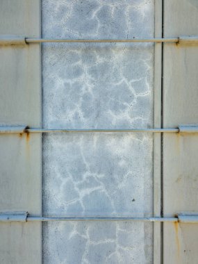 Çatlak desenli ve paslı metal çubuklu eski yüzeyi gösteren desenli beton bir bölümün detaylı görüntüsü. Duvarda yıpranma ve ışık lekesi belirtileri var. Endüstriyel ve kentsel bir doku oluşturuyor..