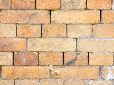 Yıpranmış sarı ve turuncu tuğlalı duvarın kumaş ve detaylarını gösteren görüntüsünü kapat. Tuğlalar görünür harç eklemleri ve yaş belirtileriyle yatay olarak dizilmiş. Burada kimse yok, bu da arka plan için uygun hale getiriyor.