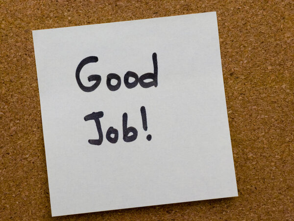 Рукописная липкая записка с мотивационной фразой "Хорошая работа", помещенная на пробковую доску объявлений, символизирующую поощрение, признание и положительную обратную связь на рабочем месте или в образовательной среде.