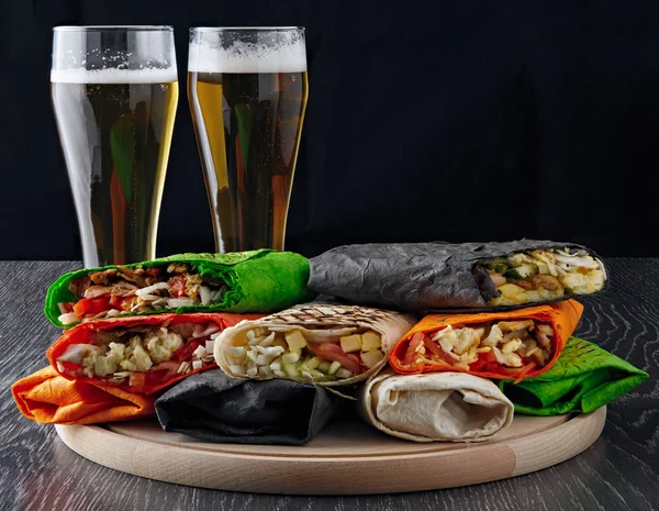 Beer in a glass and shawarma in pita bread is cut and lies on a wooden surface. The Middle Eastern dish is prepared on the grill and served with sauce.