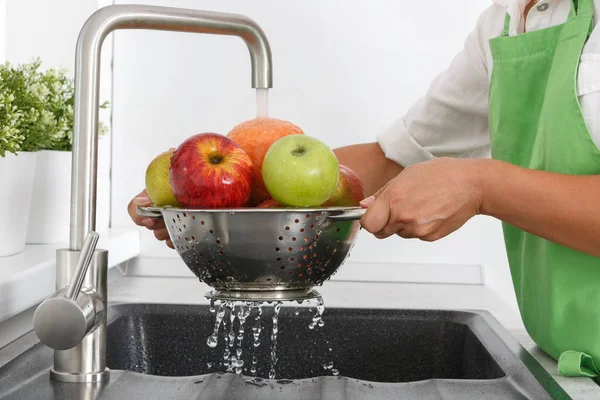 Cook woman washes fruits under running water from a water tap.