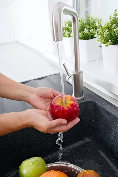 Cook woman washes an apple under running water from a water tap.