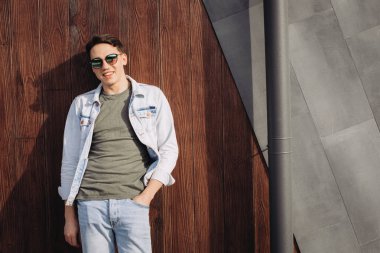 Duvar yanında güneş gözlüğüyle poz veren genç adam