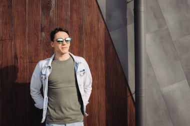 Duvar yanında güneş gözlüğüyle poz veren genç adam