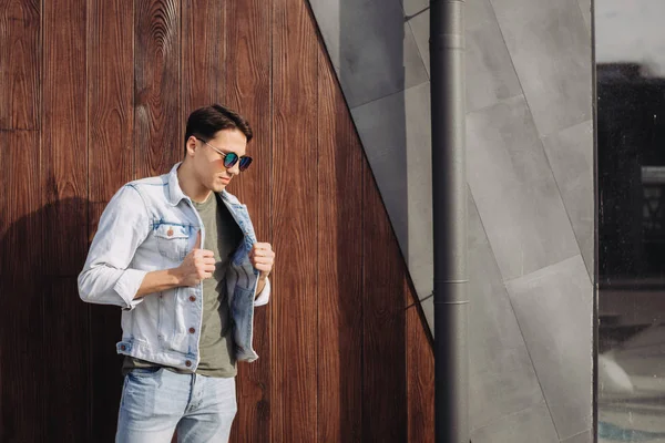 Joven posando en sus gafas de sol junto a la pared — Foto de Stock