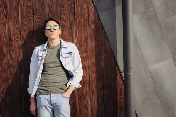 Ung man poserar i sina solglasögon bredvid väggen — Stockfoto
