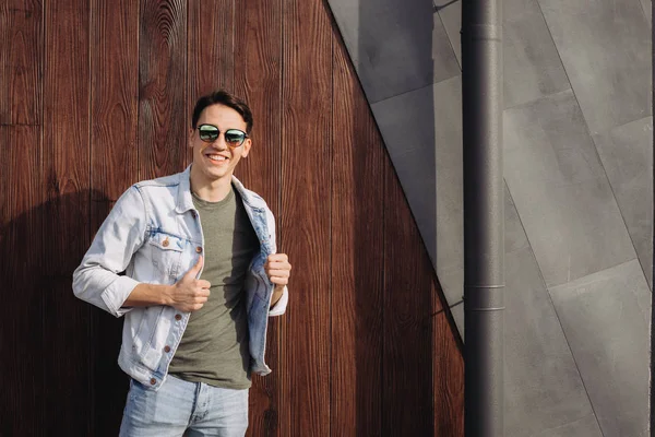 Joven posando en sus gafas de sol junto a la pared — Foto de Stock