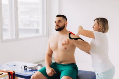 Yaralı Omuzlara Kinesio bant uygulayan fizyoterapist