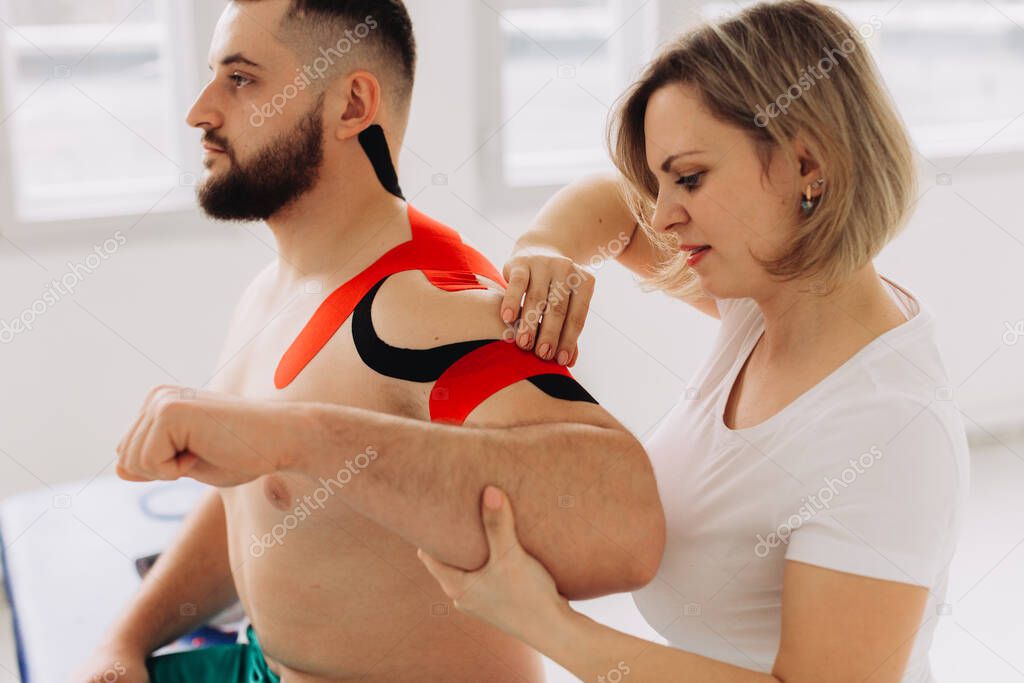 Physiotherapist Applying Kinesio Tape To Patients Injured Shoulder