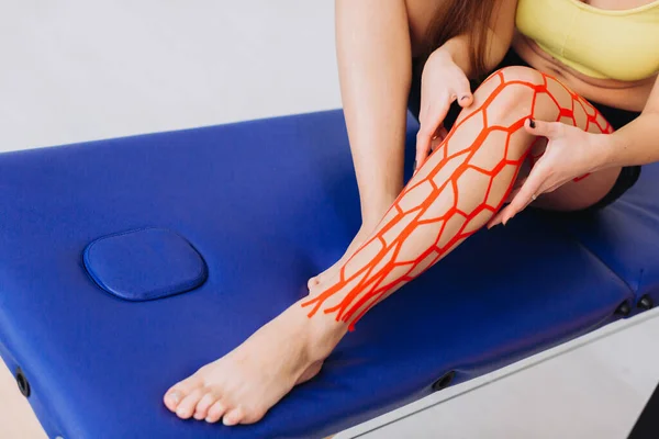 Young sportive female athlete holding her injured leg after treatment with kinesio tape. Kinesiology, physical therapy, rehabilitation concept