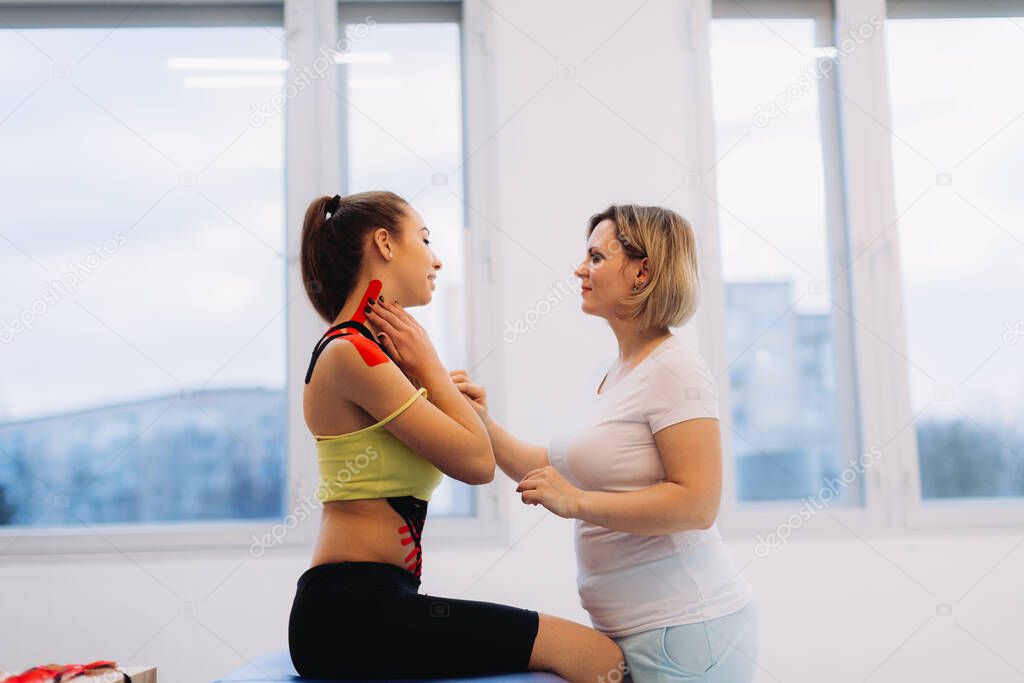 Physical therapist placing kinesio tape on woman patient's shoulder and neck