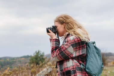 Genç bir kadın eski fotoğraf makinesiyle fotoğraf çekiyor.
