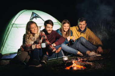 Bir grup arkadaş ateşin yanında oturuyorlar.