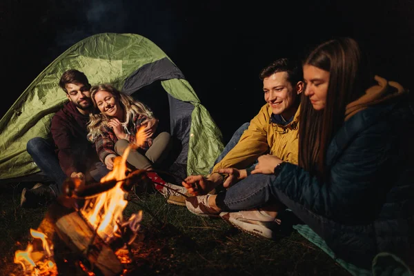 friends travelers sitting in front of bonfire at night