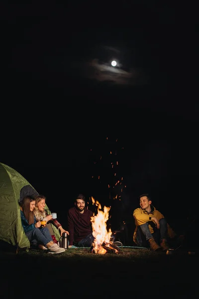 friends travelers sitting in front of bonfire at night