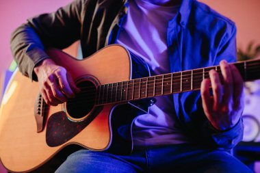 Evde müzik besteleyen genç bir müzisyen, akustik gitar çalıyor ve rahat ve yaratıcı bir atmosferde notalar yazıyor.