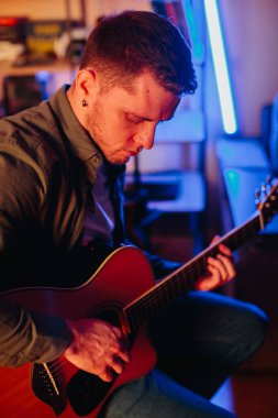 Evde oturan genç müzisyen, akustik gitarını ustalıkla çalarken yeni bir müzik bestelerken, ilham verici bir atmosferle çevrili.