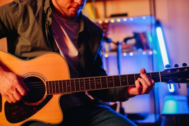 Konforlu bir ev stüdyosunda akustik gitar çalarken müzik besteleyen genç adam, şarkı yazma tutkusuna ve yaratıcılığına dalmış.