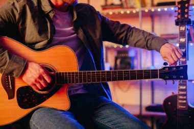 Genç müzisyen rahat bir ev stüdyosunda akustik gitarını akort ediyor, içten melodiler bestelemeye ve yaratıcılığını ifade etmeye hazırlanıyor.