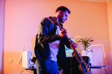 Yeni müzik besteleyen genç müzisyen renkli neon ışıkları olan bir stüdyoda elektro gitar çalıyor.