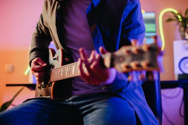 Genç müzisyen ev stüdyosunda bir şarkı besteleyip, elektro gitar çalıyor ve bilgisayar kullanıyor.