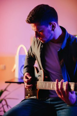 Yaratıcılık ve tutkuya dalmış, rahat bir kayıt stüdyosunda elektro gitar çalarken yeni müzik besteleyen genç bir erkek müzisyen.