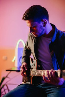 Yeni müzik besteleyen genç müzisyen, neon ışıklarıyla ev kayıt stüdyosunda elektro gitar çalıyor.
