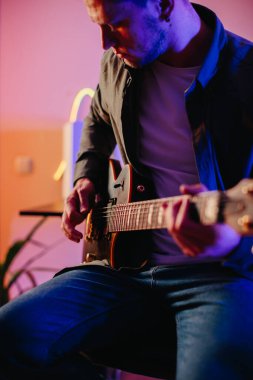 Müzik besteleyen genç müzisyen, neon ışıkları olan bir stüdyoda elektro gitar çalıyor.