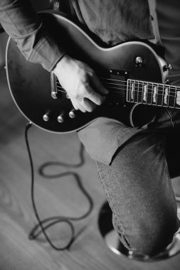 Genç müzisyen evdeki taburede oturmuş, elektro gitar çalarken yeni bir müzik besteliyor, yaratıcılık ve tutkuya dalmış.