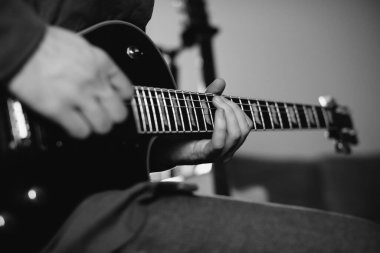 Elektro gitarı ustalıkla çalan ellerin yakın çekimi, çarpıcı bir siyah beyaz imge ile tutkuyla yeni bir şarkı bestelemesi