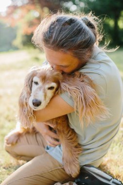 Parkta yaşlı köpeğini kucaklayan ve öpen bir adam yaşlı evcil hayvanına sevgi ve ilgi gösterir.