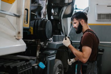 Profesyonel bir tamirci, bir garaj atölyesinin içinde bir kamyon motoru üzerinde çalışıyor, uygun bakım ve onarım için araçlar ve uzmanlık kullanıyor.
