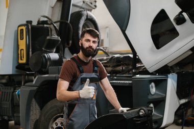 Profesyonel oto tamircisi, bir kamyon motorunu başarıyla tamir ettikten sonra, garajdaki işinden memnun olduğunu belirterek baş parmağını kaldırdı.