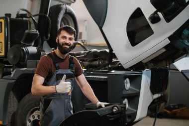 Gülümseyen tamirci garajda bir kamyonu tamir ederken başparmak gösteriyor, başarılı bir bakım işi.
