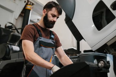 Otomobil tamircisi bir garaj atölyesinin içinde bakım ve onarım yapan bir kamyon motoru üzerinde çalışıyor.