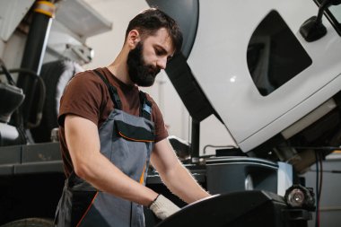 Profesyonel oto tamircisi garajda bir kamyon motoru üzerinde çalışıyor, bakım ve onarım yapıyor.